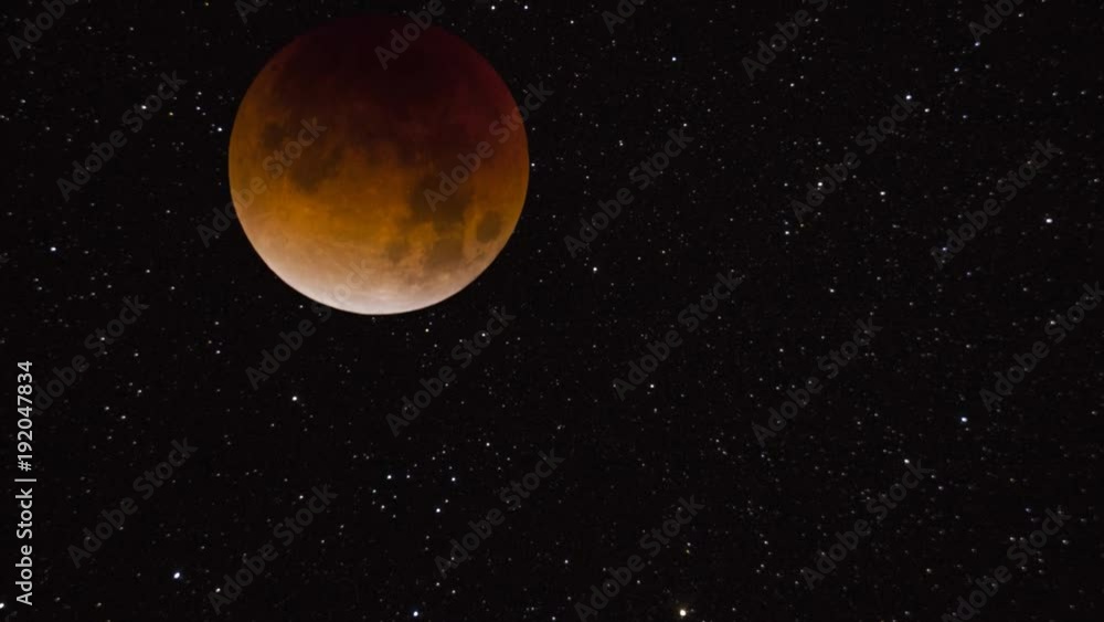 A total lunar eclipse moving across a starry sky