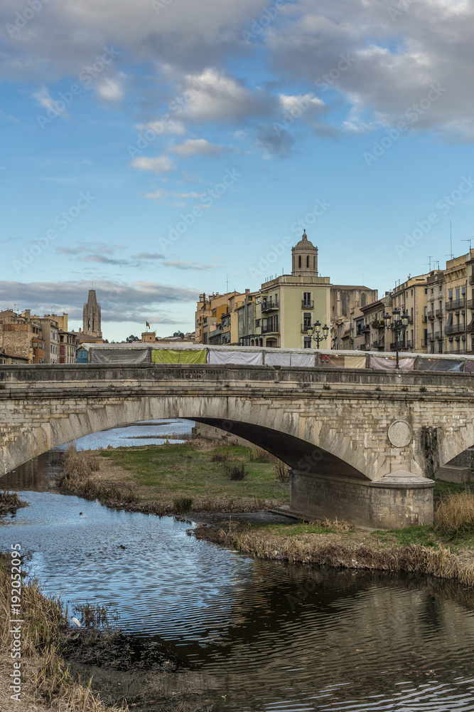 Girona cityscape with stone bridge landmark over Onyar river on a cloudy and sunny day
