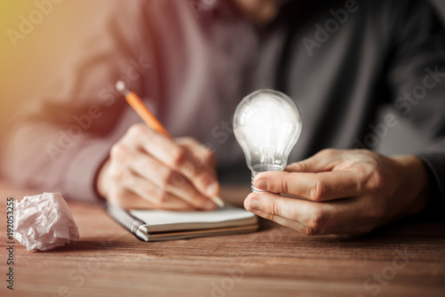 Картината върху платно Businessman holding light bulb and writing down in the notebook new creative ideas