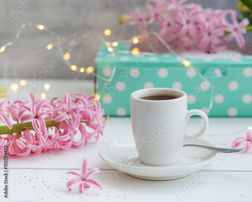 Cup of coffee with pink hyacinths on the wooden background with garland. Spring postcard concept.