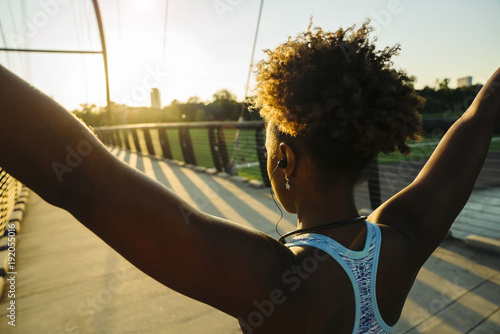 Mixed Race woman wearing earbuds stretching arms on bridge