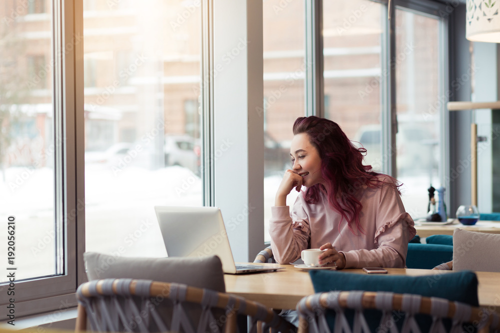 A beautiful charming girl using her mobile phone and laptop in cafe with sun shines through the window. Woman, technology outdoors concept A beautiful charming girl using her mobile phone and laptop in cafe with sun shines through the window. Woman, technology outdoors concept