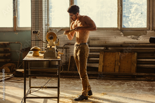 Turner working on a lathe in the workshop. Male hand carved wooden blank photo