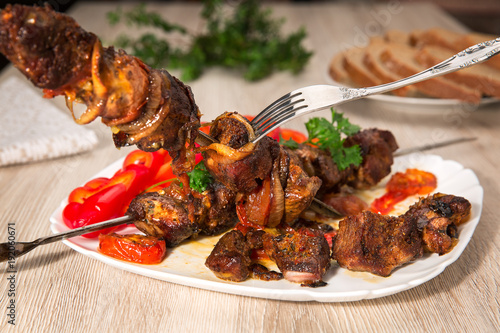 Kebabs on skewers. Roasted meat, tomatoes, pepper, parsley and onion on the white dish on the wooden table.