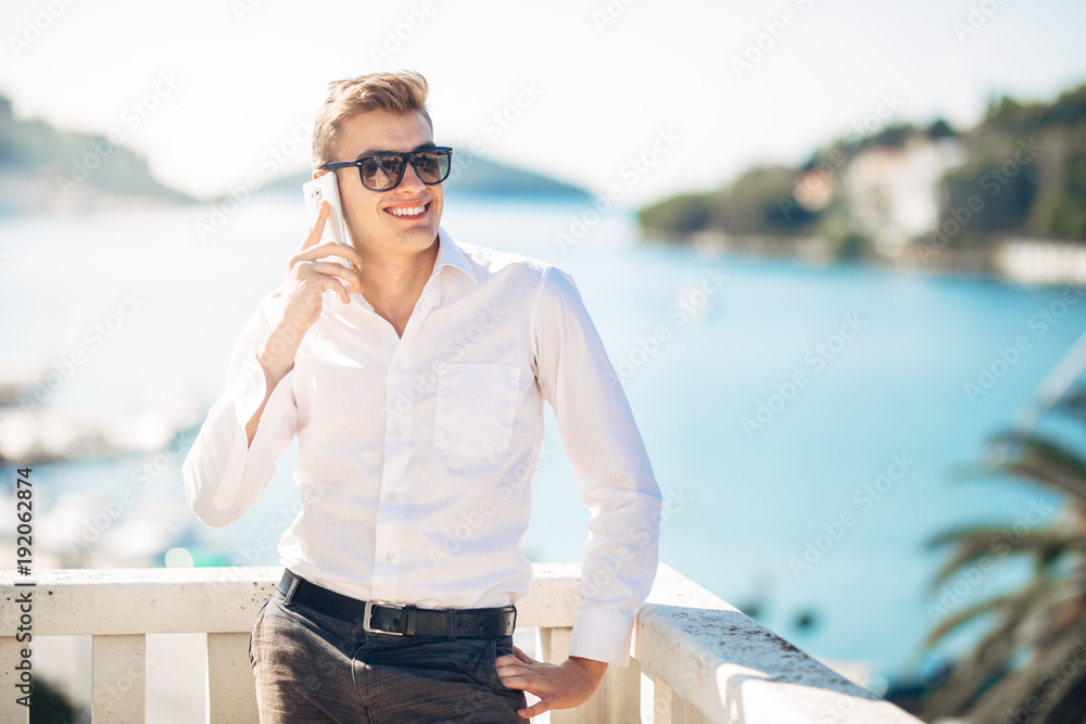 Young handsome man enjoying stay at luxury resort hotel with panoramic view on the sea.Smiling business man using his smartphone options at a earned tropical vacation.Business traveling.Outsourcing
