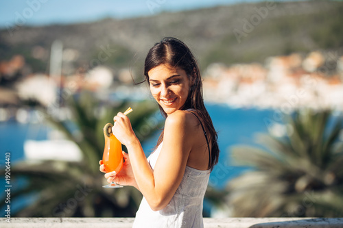 Young female enjoying a colourful cocktail on the panoramic view hotel terrace.Cold delicious cocktail smoothie for the summer hot days.Enjoying summer vacation.Happy female relaxing.Drinking alcohol