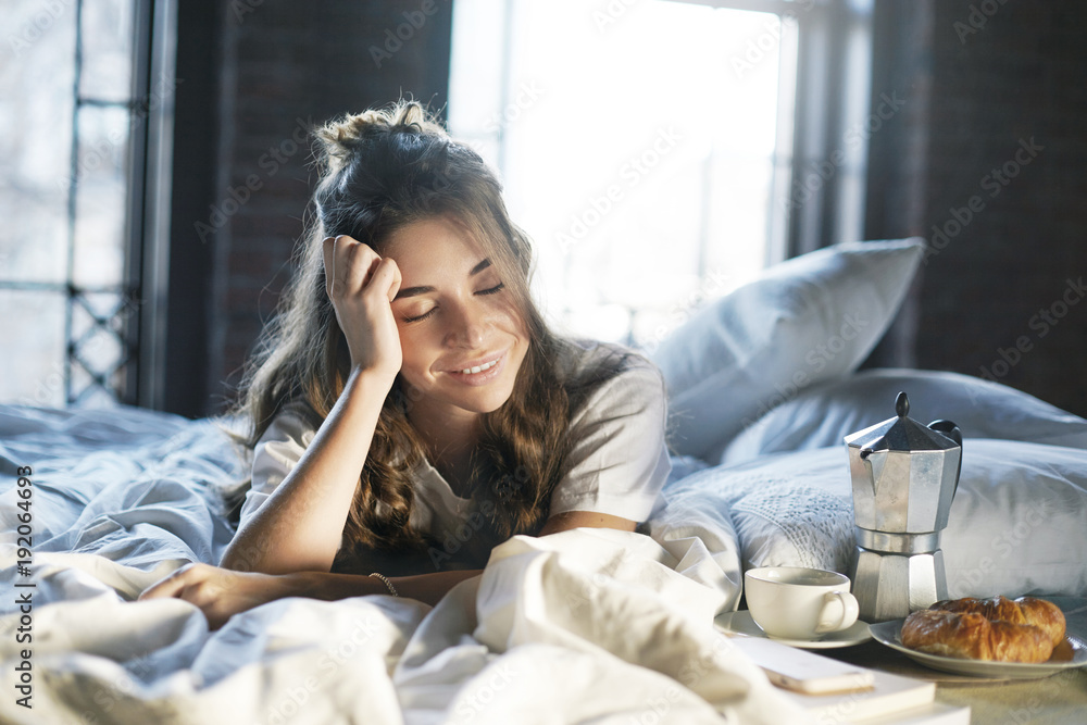 Picture of joyful lazy young woman with messy hair lying awake in bedroom  after good sleep,