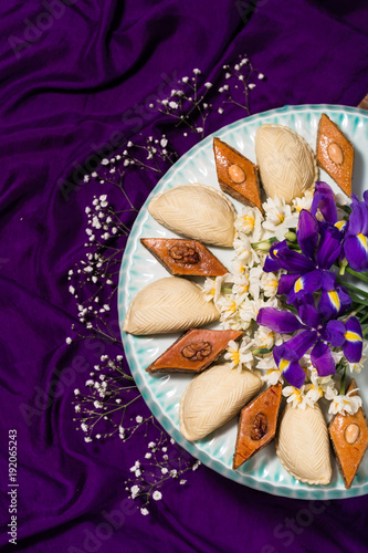 Novruz celebration plate with traditional national pastries in Azerbaijan - shekerbura and pakhlava decorated with spring  flowers daffodils and purple fleur de lis silk purple background copy space photo