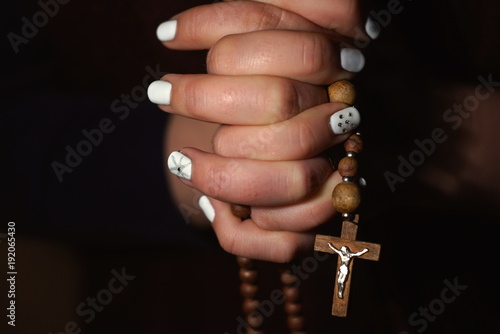 Hands folded in prayer on a black background. Rosary in the hands of woman