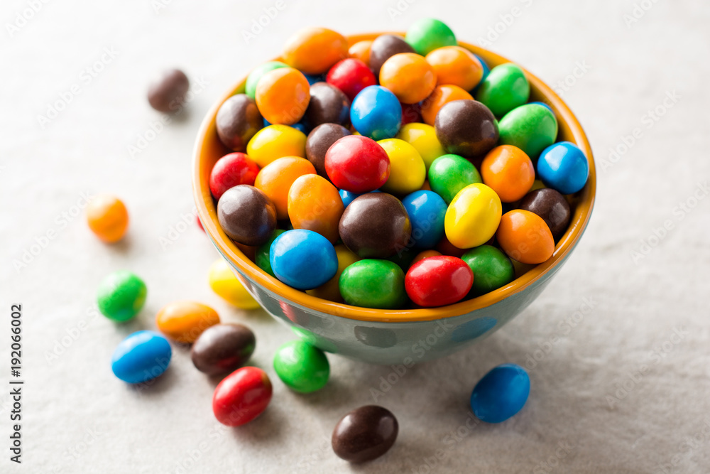 Colorful chocolate buttons in bowl on gray stone background.
