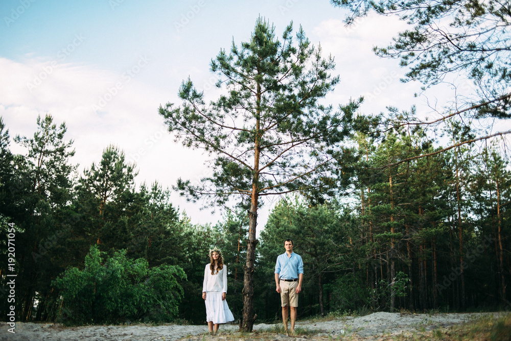 Beautiful photo of an attractive couple who stands in a forest near a pine-tree Beautiful photo of an attractive couple who stands in a forest near a pine-tree