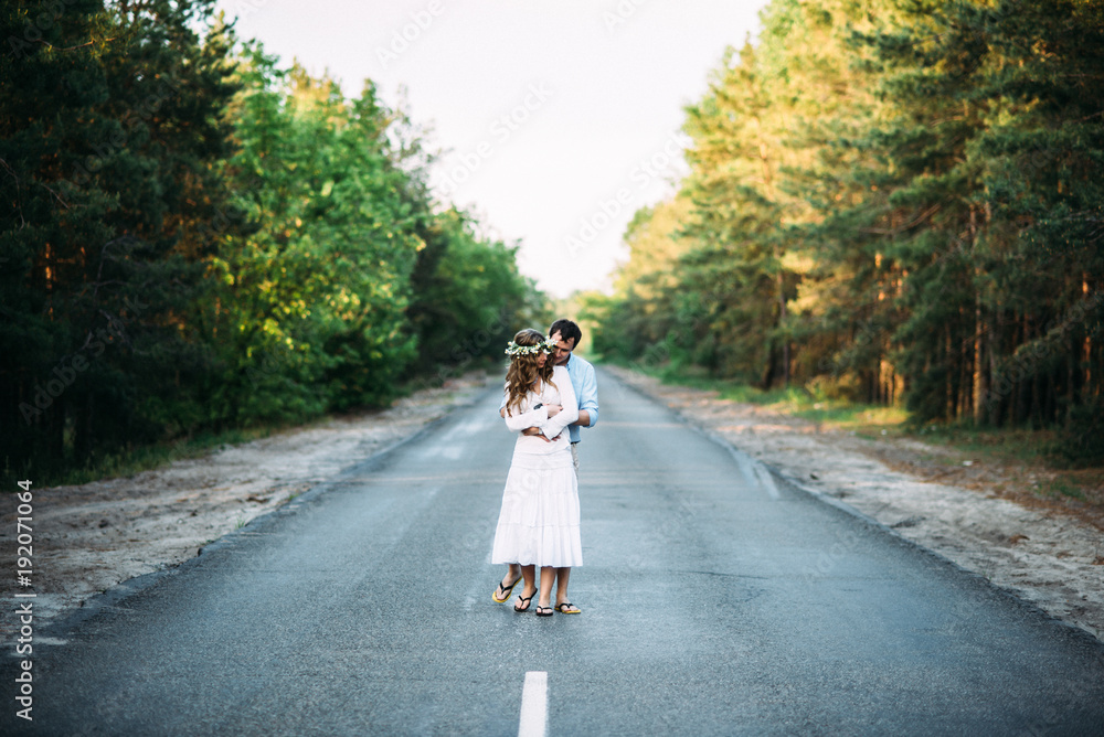 Loving happy couple hugging on the road in the forest at sunset