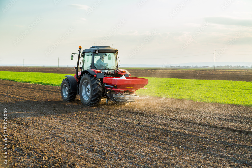 Fototapeta premium Farmer fertilizing arable land with nitrogen, phosphorus, potassium fertilizer