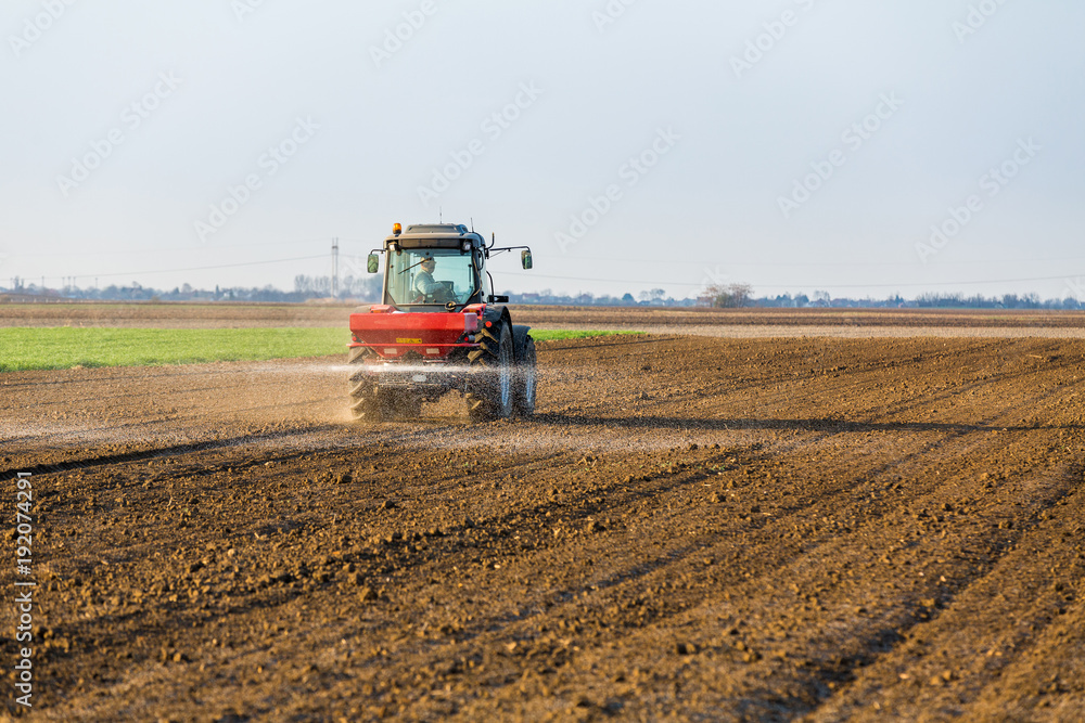 Fototapeta premium Farmer fertilizing arable land with nitrogen, phosphorus, potassium fertilizer
