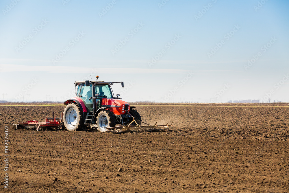 Fototapeta premium Farmer in tractor preparing land with seedbed cultivator as part of pre seeding activities in early spring season of agricultural works at farmlands.
