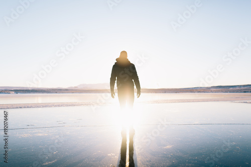 Man walks with his reflection following on frozen lake in the Golden Circle in Iceland