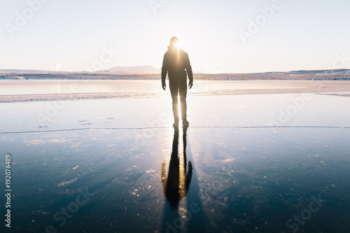 Man walks on a frozen lake in the Golden Circle in Iceland with reflection following