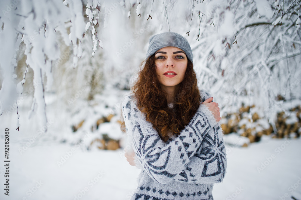 Cute curly girl in sweater and headwear at snowy forest park at winter. Cute curly girl in sweater and headwear at snowy forest park at winter.