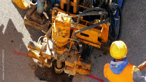 Drilling rig industry. Hydraulic worker dressed in yellow helmet and working clothes operating drilling machinery. Man fixing long metal rotary pipes for further explorations