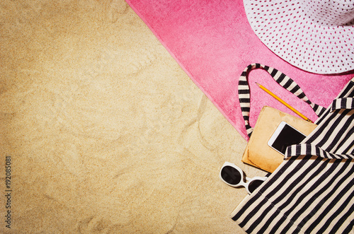 Top view of sandy beach with towel frame and summer accessories. Background with copy space and visible sand texture. Border composition made of towel