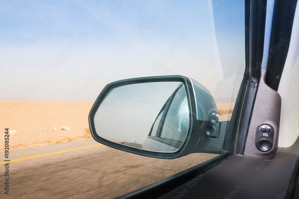Car mirror, road and yellow desert around in a summer