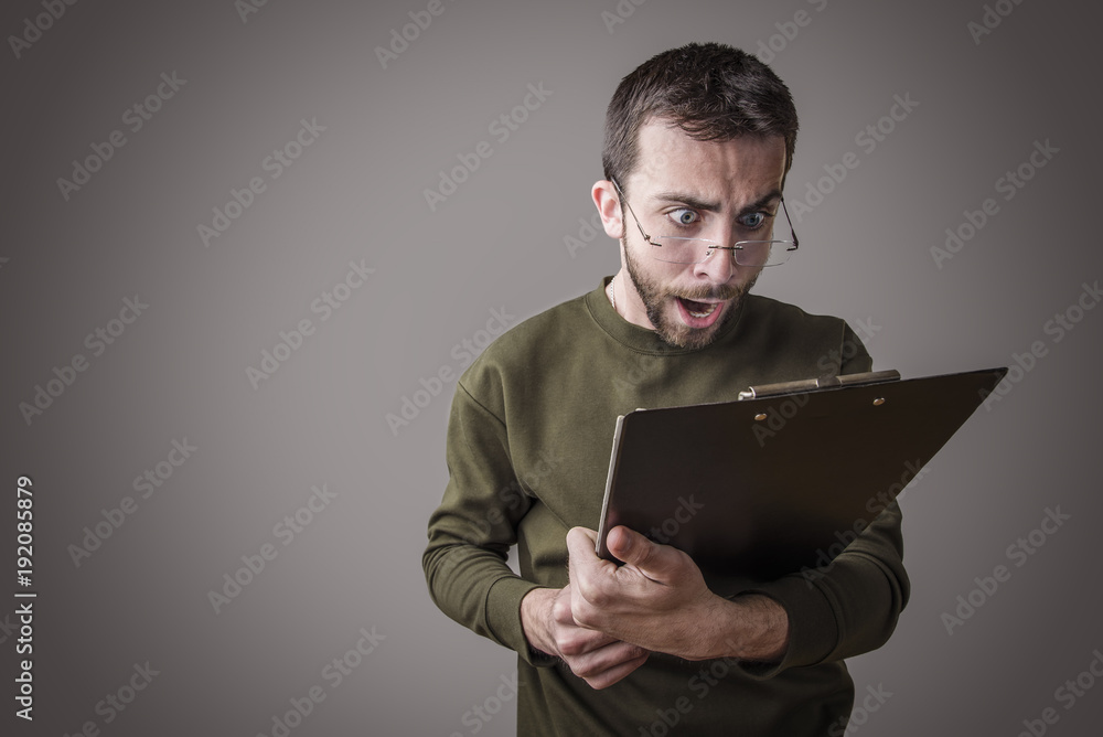 Young man is in shock with his finances and reports, holding his spectacles Young man is in shock with his finances and reports, holding his spectacles