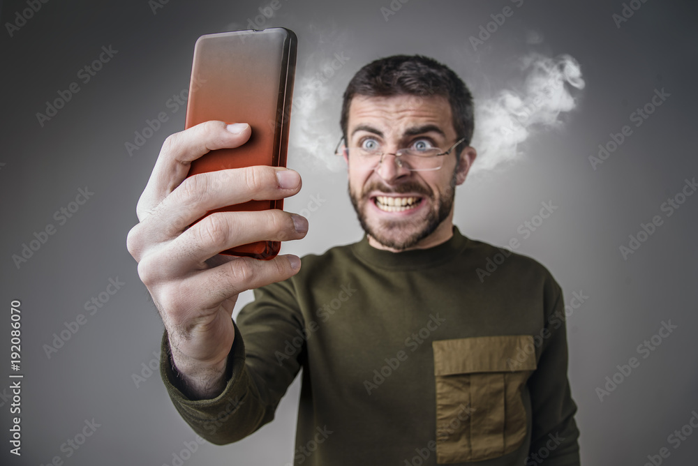 Young man angry with his cell phone, yelling at it, letting off steam and burning his phone with rage - obrazy, fototapety, plakaty 