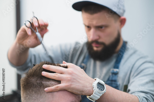 Hairdresser with beard cuts hair with scissors and a comb. Create a stylish men's hairstyle in barbershop.