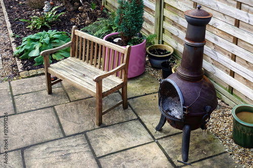 Wooden bench, chiminea and various plants, some in pots, in a small domestic courtyard garden in winter