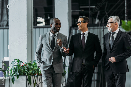 smiling multiracial businessmen having conversation while walking in office photo