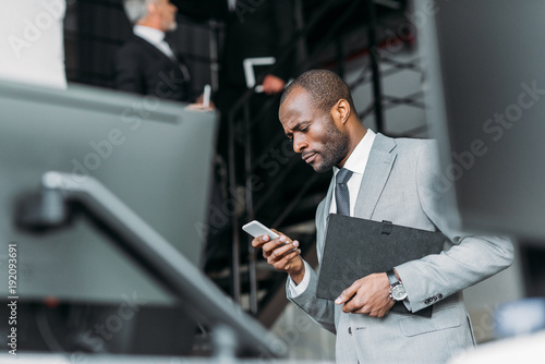 selective focus of african american businessman with documents using smartphone