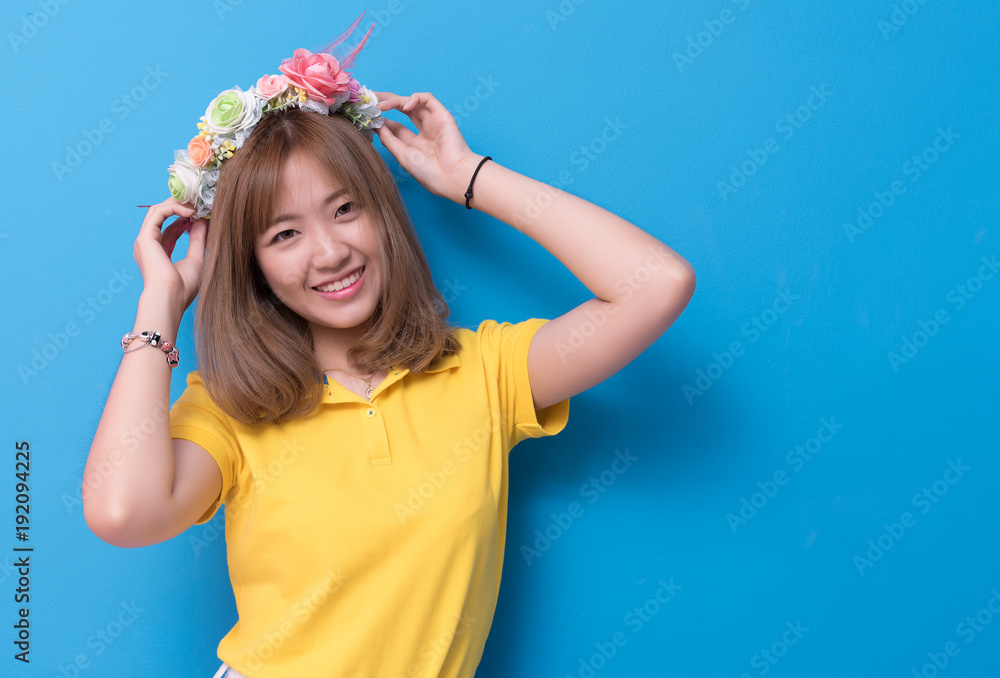 Beauty woman posing with flower hat in front of blue wall background. Summer and vintage concept. Happiness lifestyle and people portrait theme. Cute gesture and pastel tone. Beauty woman posing with flower hat in front of blue wall background. Summer and vintage concept. Happiness lifestyle and people portrait theme. Cute gesture and pastel tone.