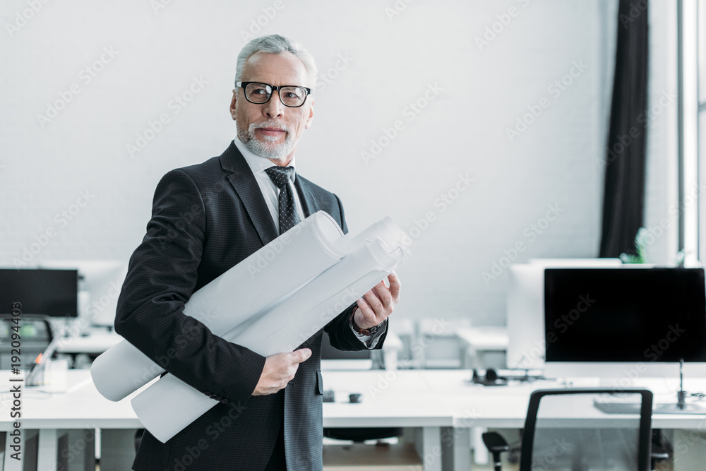 portrait of senior businessman with blueprints in office