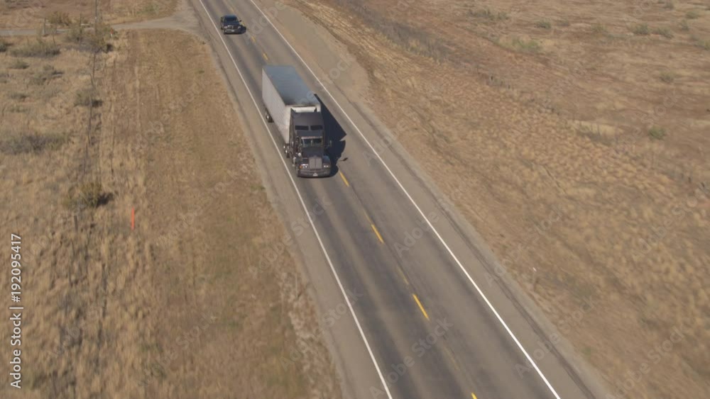 AERIAL Flying above freight container semi-trailer truck transporting goods across the country highway passing through deserted landscape in Utah, United States. Logistics, transport & shipping cargo AERIAL Flying above freight container semi-trailer truck transporting goods across the country highway passing through deserted landscape in Utah, United States. Logistics, transport & shipping cargo
