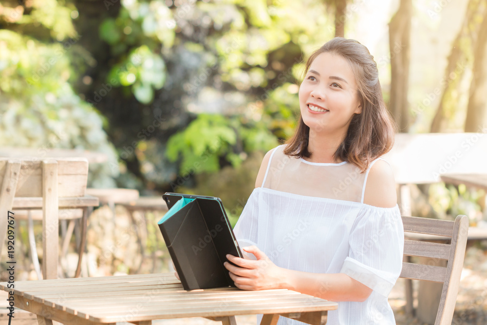 Portrait of Attractive young Asian woman wearing white casual using tablet smiling and thinking about something good. Technology, Internet, and Business concept. Portrait of Attractive young Asian woman wearing white casual using tablet smiling and thinking about something good. Technology, Internet, and Business concept.