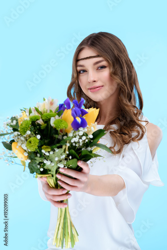 happy young woman holding floral bouquet isolated on blue