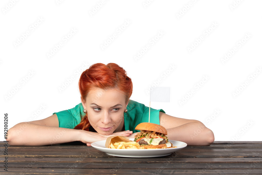 red-haired young woman looks suspiciously at hamburger on plate red-haired young woman looks suspiciously at hamburger on plate