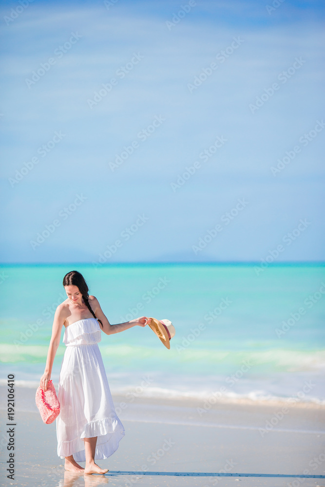Young beautiful woman on white sand tropical beach. Caucasian girl with hat in dress background the sea Young beautiful woman on white sand tropical beach. Caucasian girl with hat in dress background the sea