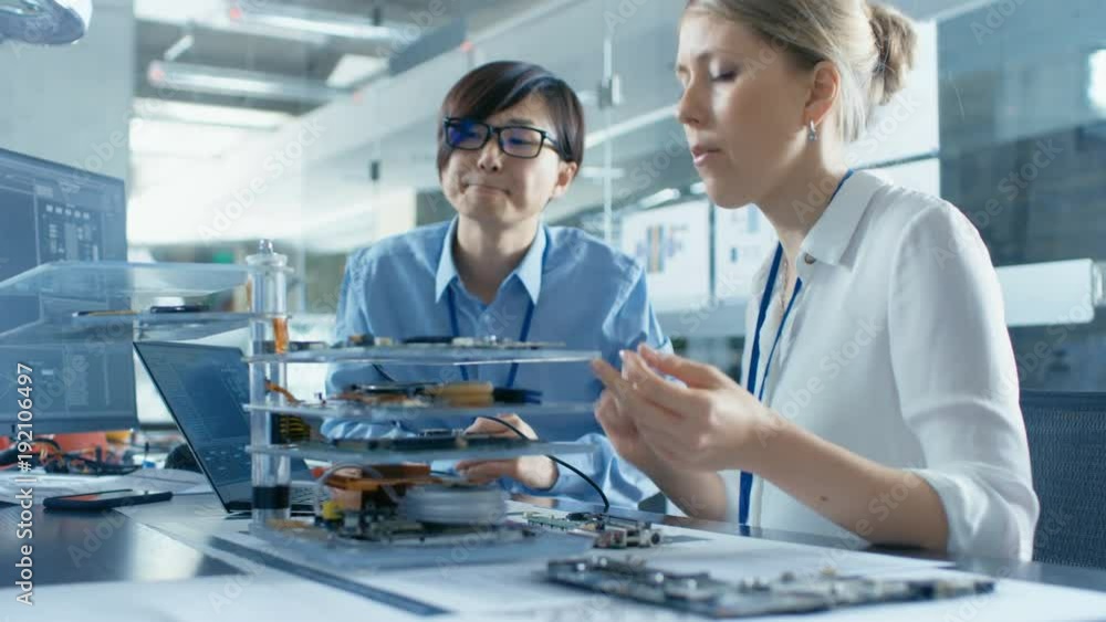 Two Computer Engineers Choose Printed Circuit Boards to Work with. In The Background Technologically Advanced Scientific Research Center. Two Computer Engineers Choose Printed Circuit Boards to Work with. In The Background Technologically Advanced Scientific Research Center.