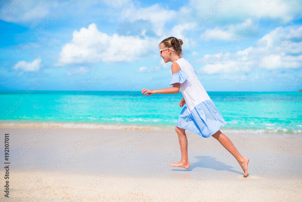 Happy little girl running and splashing at shallow water at beach having a lot of fun on summer vacation Happy little girl running and splashing at shallow water at beach having a lot of fun on summer vacation