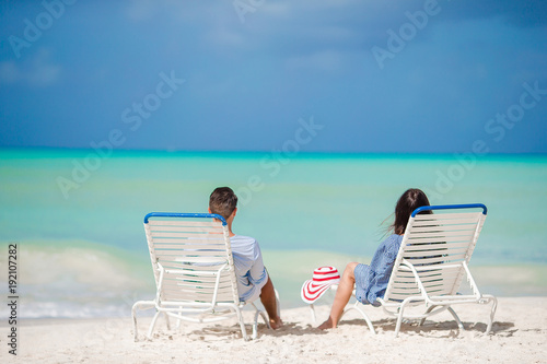 Two happy people having fun on the beach, sitting on comfortable sunbed