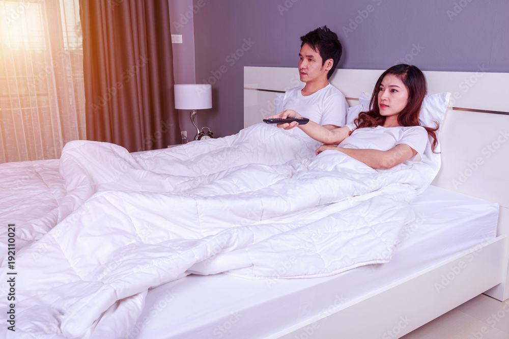 Fototapeta premium young couple lying on a bed with remote control and watching television in bedroom