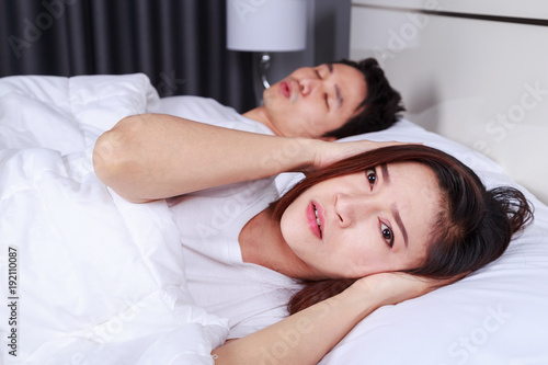 annoyed wife blocking her ears from noise of husband snoring in bedroom