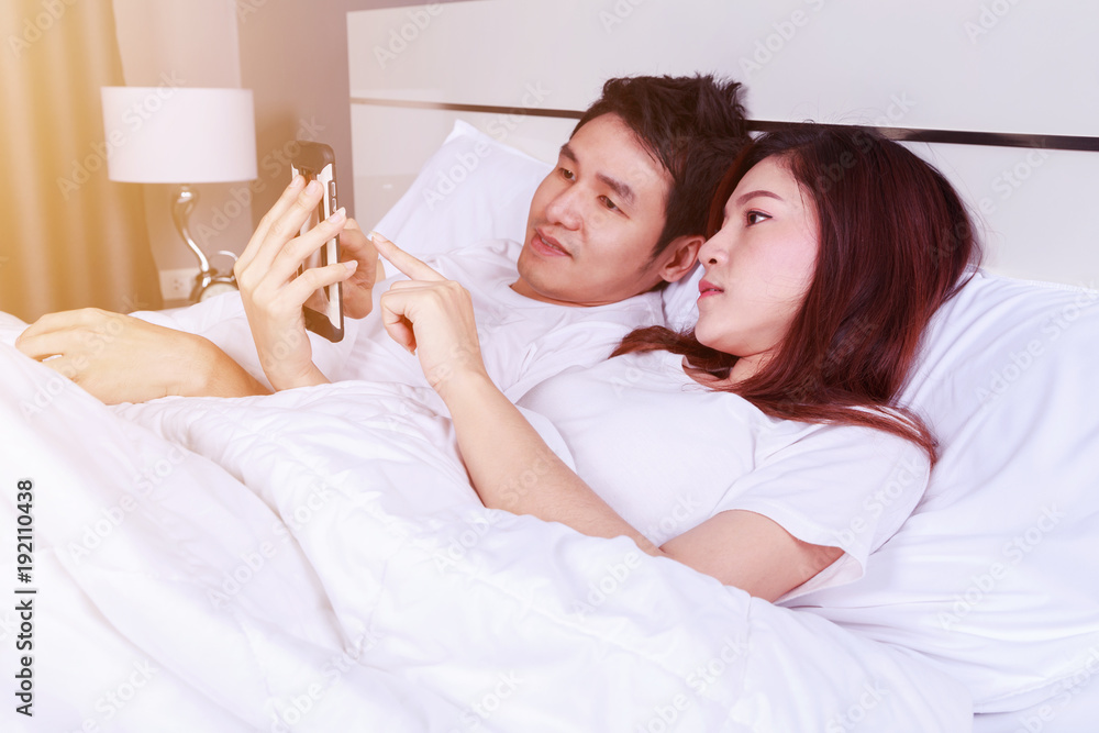 young couple using mobile phone on bed in bedroom young couple using mobile phone on bed in bedroom