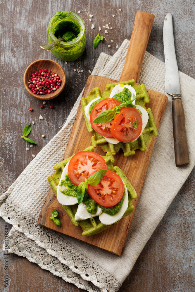 Sandwiches on green wafer with spinach and mozzarella cheese, pesto sauce, tomatoes and basil on a gray concrete old background. Selective focus. Top view. Sandwiches on green wafer with spinach and mozzarella cheese, pesto sauce, tomatoes and basil on a gray concrete old background. Selective focus. Top view.