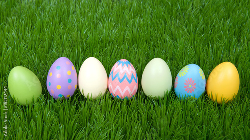 Colorful decorative and plain easter eggs lined up in a row in green grass.