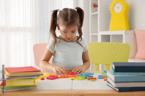 Cute little girl playing with figures while doing homework indoors