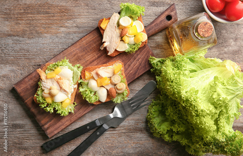 Wooden board with tasty chicken bruschettas on table