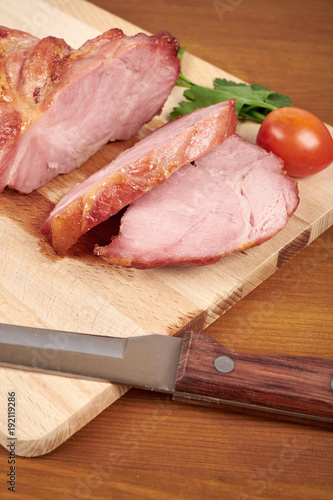 Cooked sliced pork ham steak on wooden cutting board.