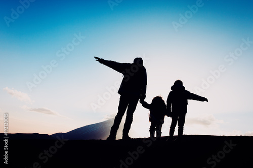 Silhouettes of happy father and two kids hiking at sunset